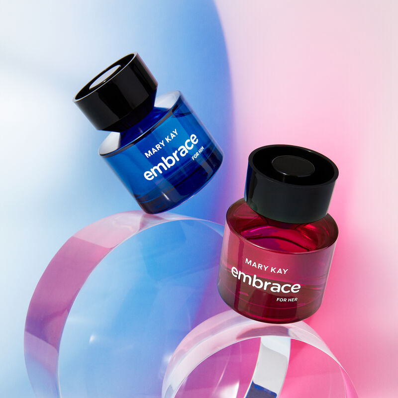Mary Kay Embrace for Him Eau de Toilette and Mary Kay Embrace for Her Eau de Toilette balancing on clear orbs against blue and pink backgrounds