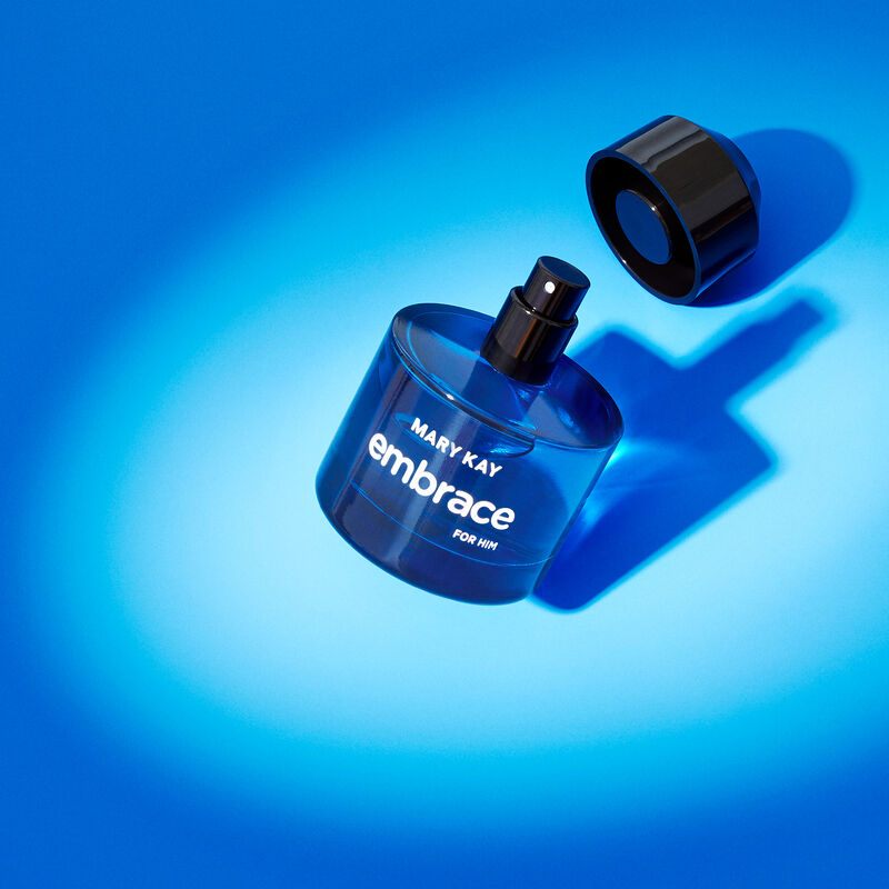 Uncapped bottle of Mary Kay Embrace for Him Eau de Toilette balancing on its edge in the spotlight against a blue background