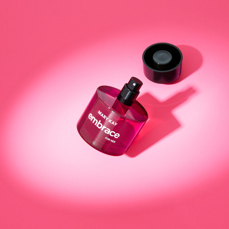 Uncapped bottle of Mary Kay Embrace for Her Eau de Toilette balancing on its edge in the spotlight against a pink background