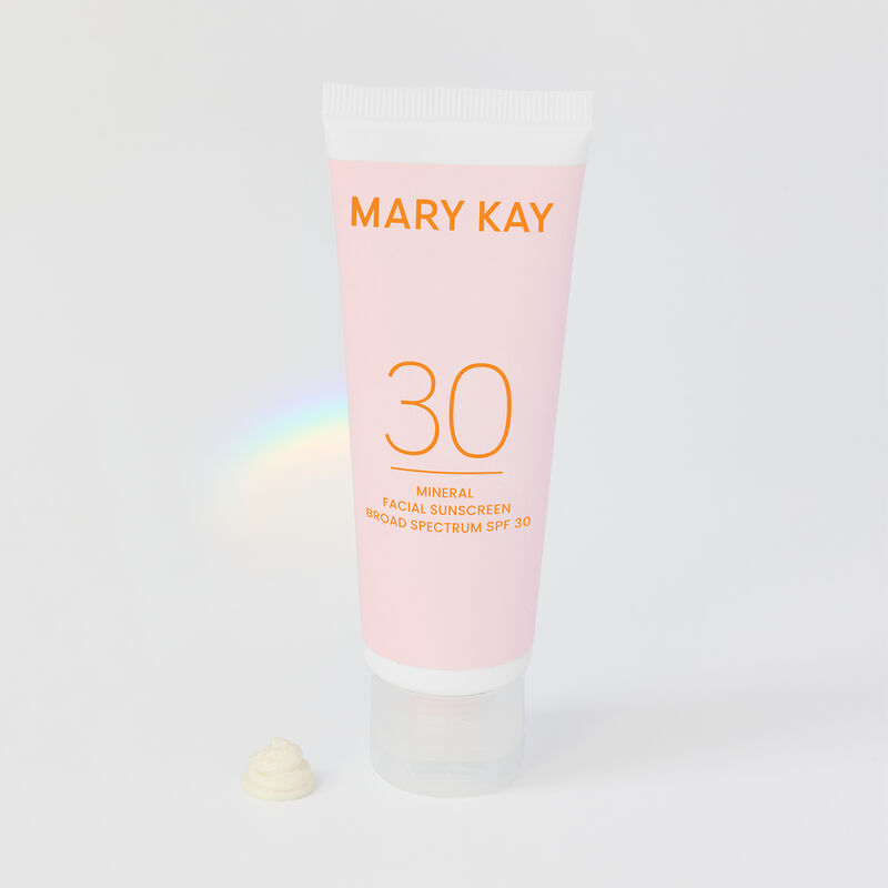 Bottle of Mary Kay Mineral Facial Sunscreen Broad Spectrum SPF 30* standing on its cap with rainbow prism in the background 