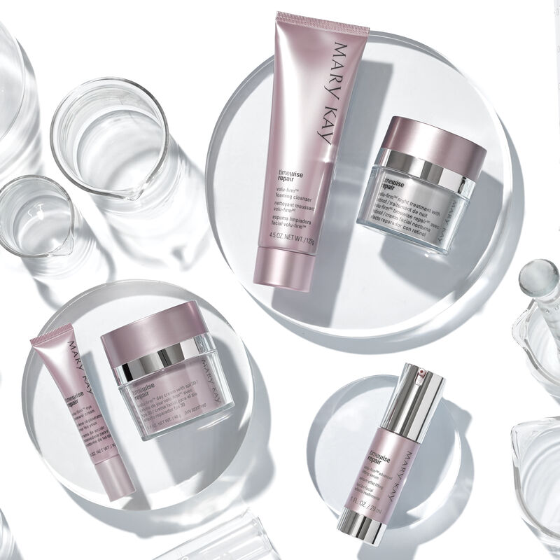 The Mary Kay TimeWise Repair Volu-Firm Set placed on glass platforms with glass scientific accessories.