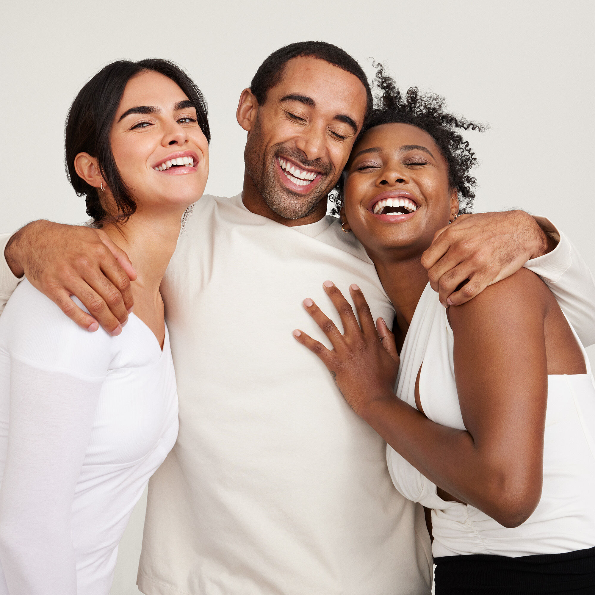 Dos mujeres y un hombre abraz&aacute;ndose y riendo, mostrando alegr&iacute;a y cercan&iacute;a.