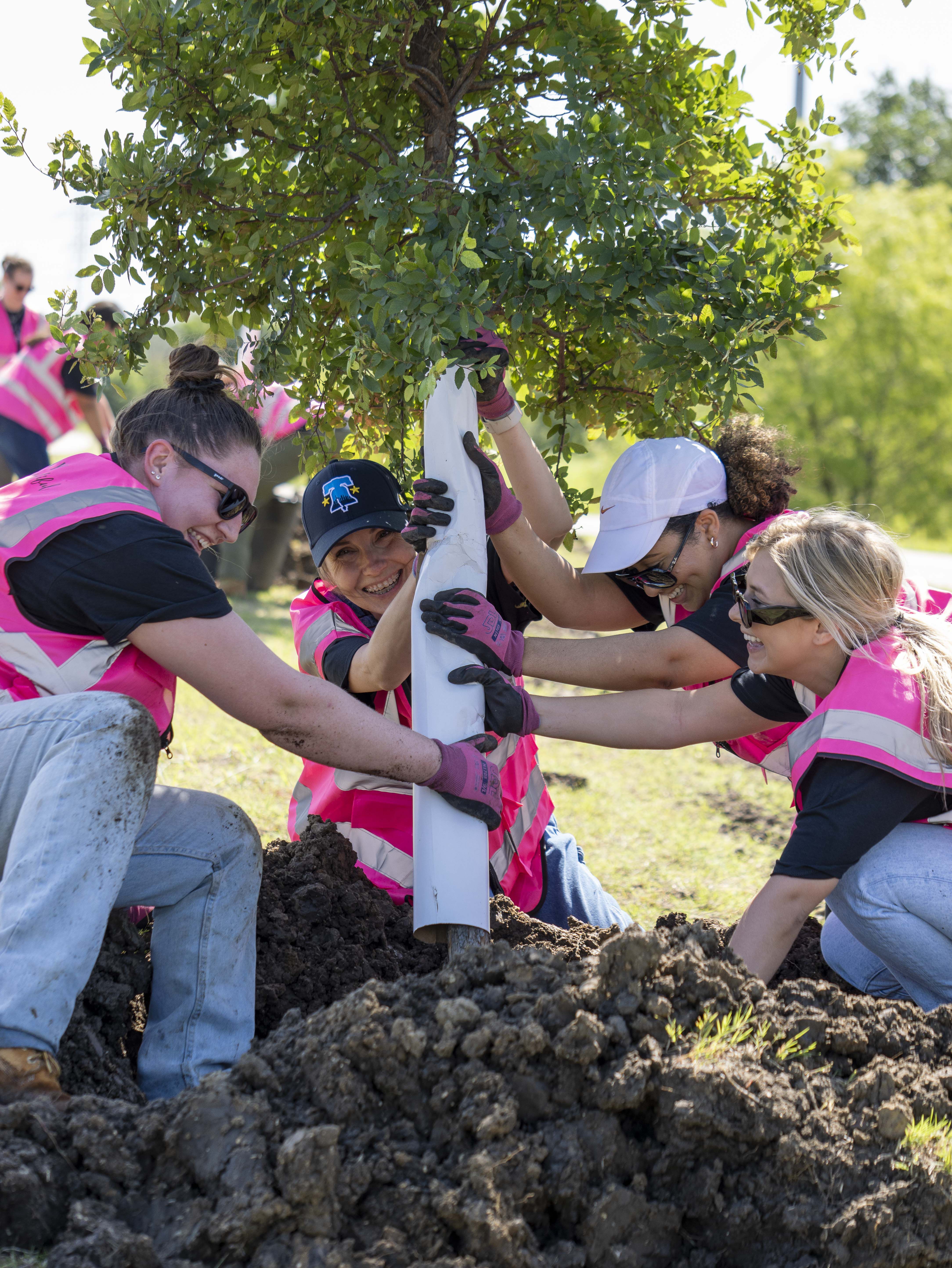 Miembros del equipo Mary Kay, con chalecos rosas, trabajando juntos para sembrar un &aacute;rbol.