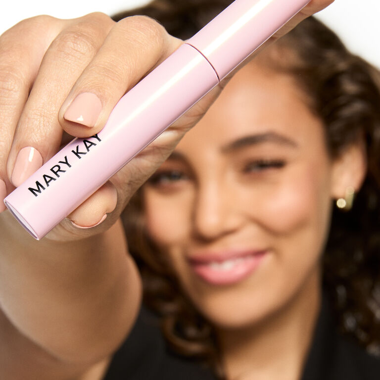 Hand holding a pink Mary Kay mascara tube with nails painted in a neutral shade.