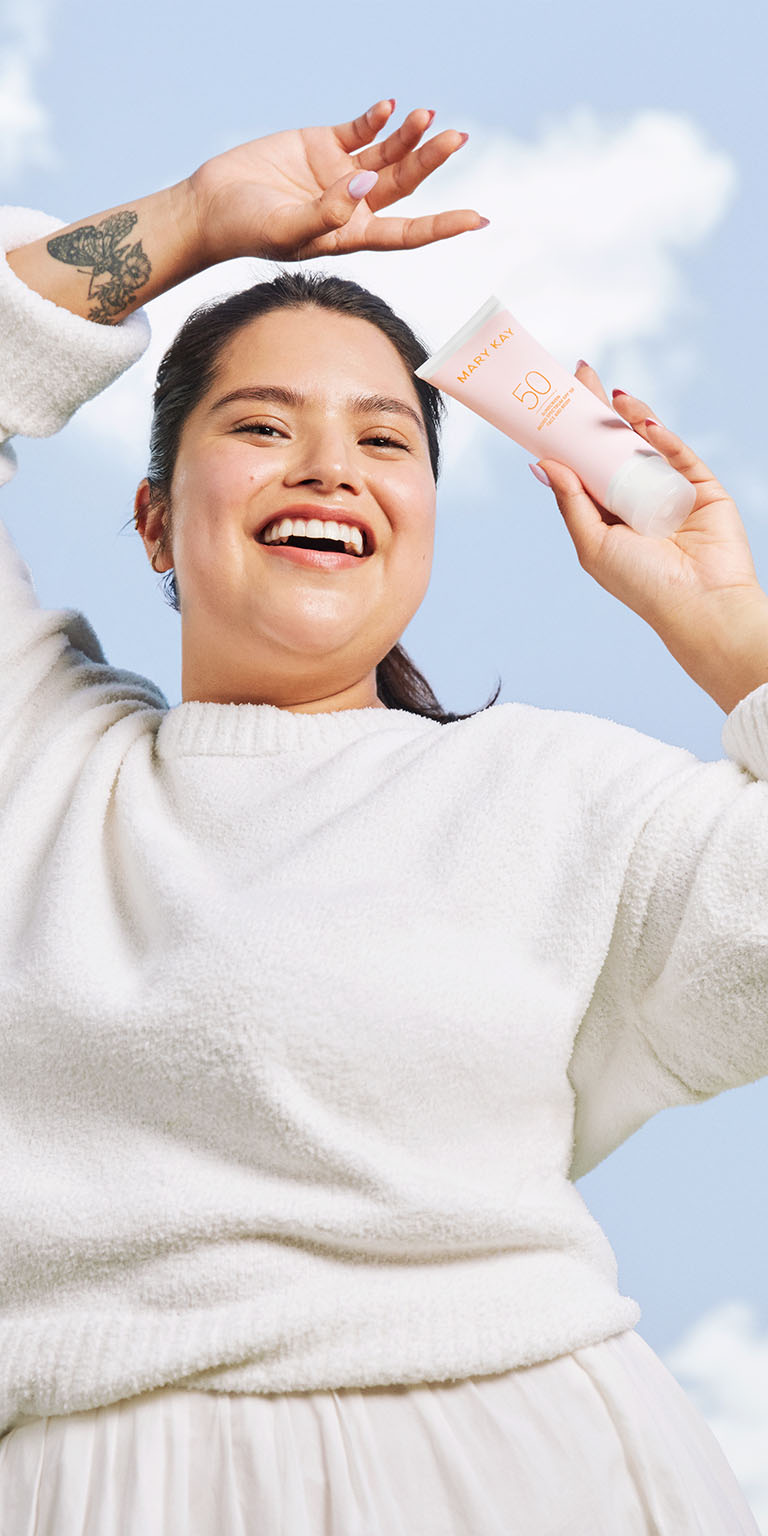 Modelo sosteniendo el protector solar Mary Kay de amplio espectro FPS 50 bajo un cielo azul.