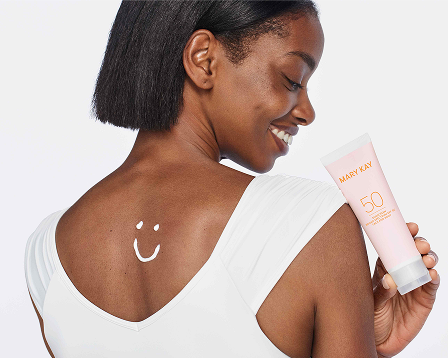 Modelo sosteniendo un tubo de Protector Solar FPS 50+ Mary Kay&reg; Protecci&oacute;n Muy Alta, con una carita sonriente dibujada con protector solar en la parte superior de la espalda.