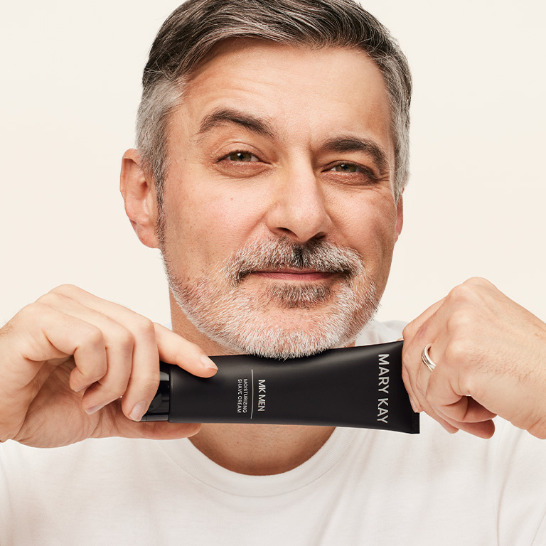 Hombre sonriendo y sosteniendo el tubo de la Crema de Afeitar MKMen&reg; junto al ment&oacute;n