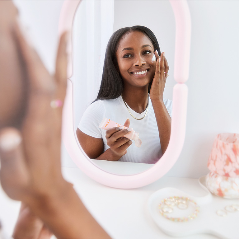 Mujer mirando en un espejo de maquillaje y aplicando Protector Solar Facial Mineral FPS 30 Mary Kay&reg; en la mejilla