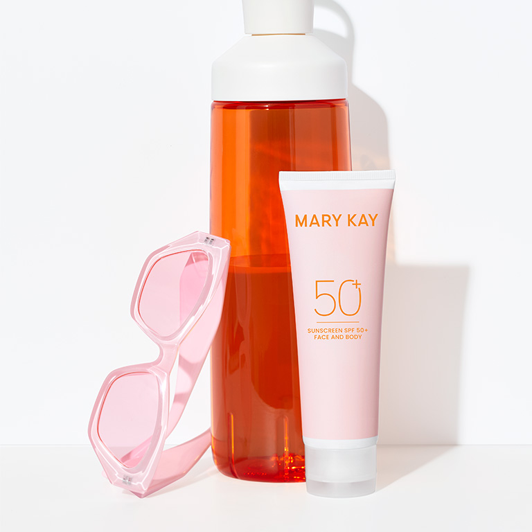 Protector solar Mary Kay de amplio espectro FPS 50 junto a una botella de agua naranja y lentes de sol rosas, ideales para el verano.